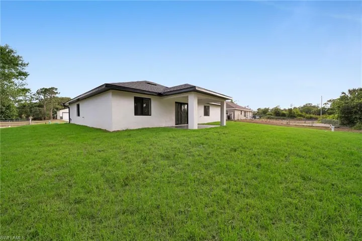 Back of house featuring a lawn, fence, and stucco siding