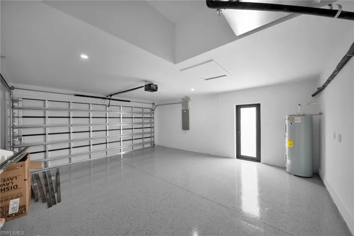Garage featuring electric panel, a garage door opener, recessed lighting, and electric water heater