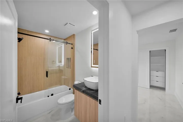 Full bath with visible vents, vanity, combined bath / shower with glass door, toilet, and marble finish floor