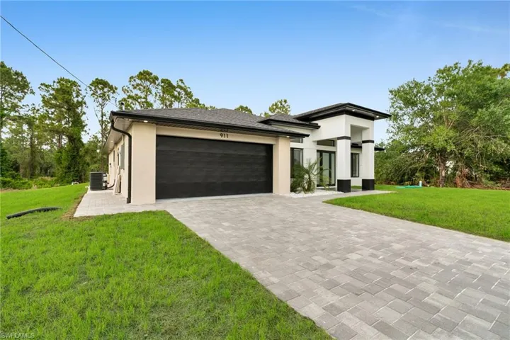 Prairie-style home with an attached garage, decorative driveway, stucco siding, and a front yard