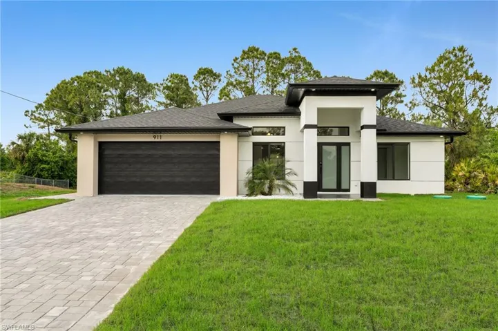 Prairie-style home with a garage, decorative driveway, fence, a front lawn, and stucco siding