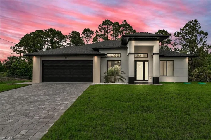 View of front facade with fence, an attached garage, stucco siding, decorative driveway, and a yard