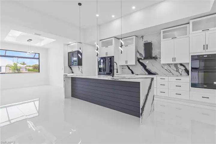 Kitchen featuring black appliances, exhaust hood, white cabinetry, a kitchen island with sink, and backsplash