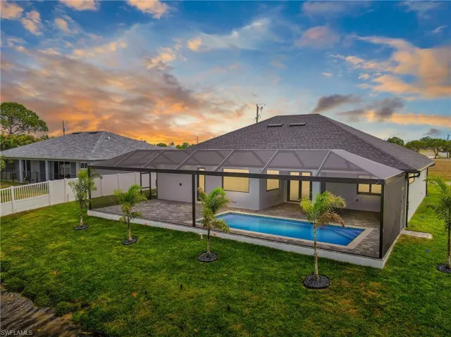 Back of property at dusk with a patio area, an outdoor pool, a fenced backyard, and a lanai