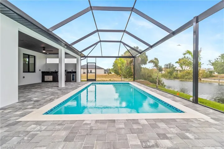 Outdoor pool with area for grilling, a patio area, a water view, glass enclosure, and a ceiling fan