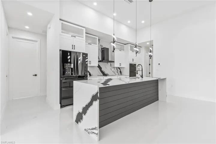 Kitchen with black appliances, wall chimney exhaust hood, white cabinetry, recessed lighting, and decorative backsplash
