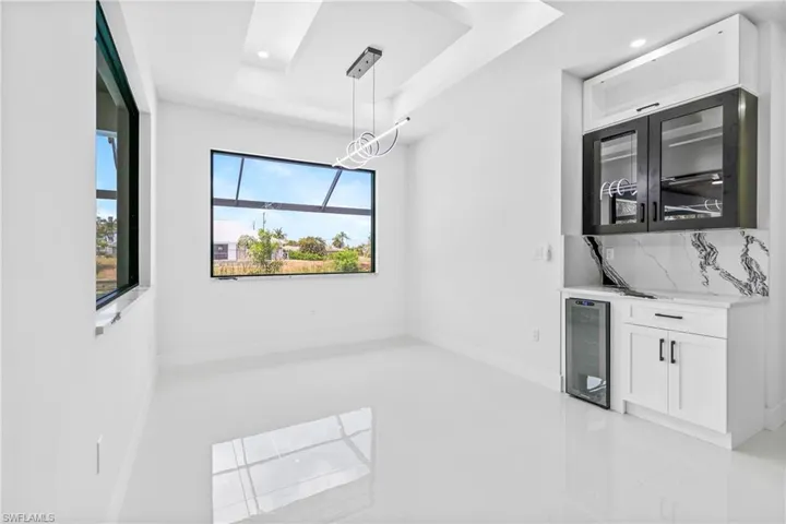 Unfurnished dining area with wine cooler, a raised ceiling, light tile patterned floors, bar area, and recessed lighting