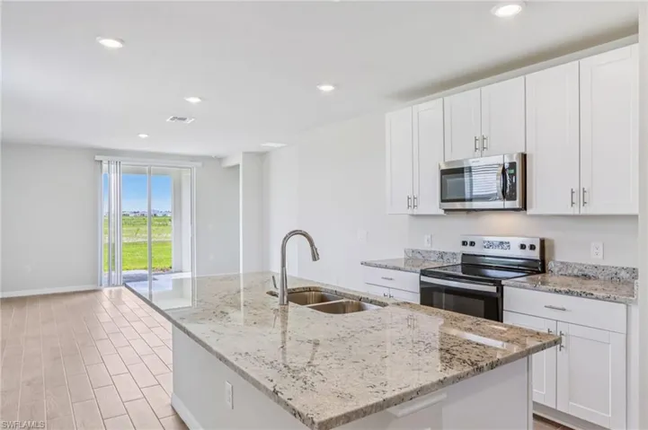 Kitchen with stainless steel appliances, a sink, a kitchen island with sink, white cabinetry, and recessed lighting