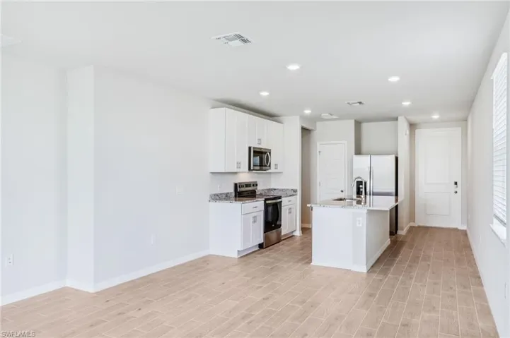 Kitchen featuring appliances with stainless steel finishes, light wood-type flooring, a kitchen island with sink, recessed lighting, and baseboards