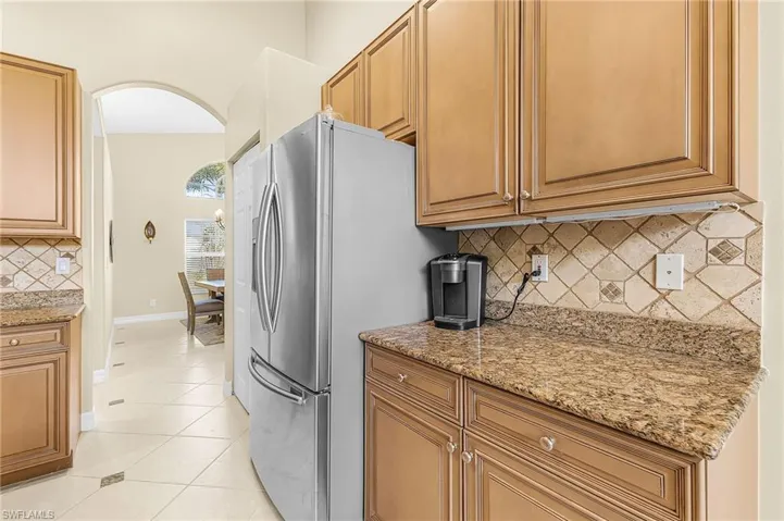 Kitchen with wood cabinetry, stainless steel refrigerator, granite countertops, and tiled backsplash