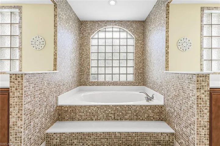 Built-in tub with mosaic tile surround, arched glass block window, and dual privacy windows