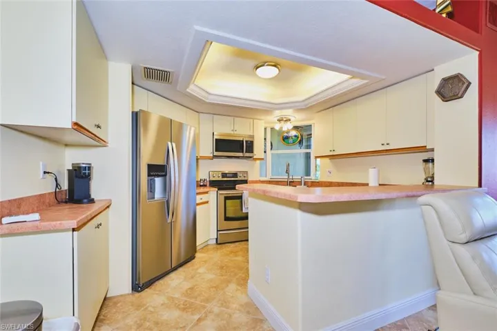 Kitchen featuring appliances with stainless steel finishes, a peninsula, a tray ceiling, light countertops, and light tile patterned flooring