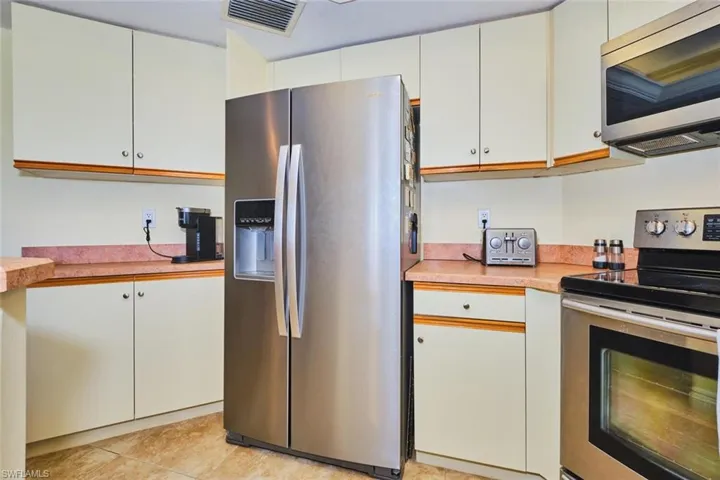 Kitchen featuring appliances with stainless steel finishes, light countertops, light tile patterned floors, and white cabinetry