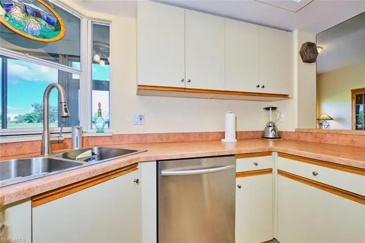 Kitchen featuring stainless steel dishwasher, light countertops, and white cabinets