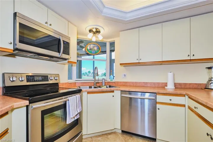 Kitchen featuring stainless steel appliances, light countertops, ornamental molding, white cabinetry, and light tile patterned floors