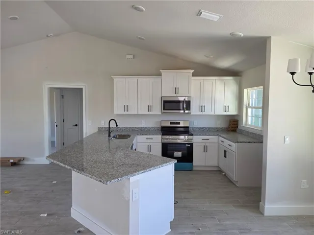 Kitchen featuring white shaker cabinetry, stainless steel appliances, granite countertops, and a central island with an undermount sink