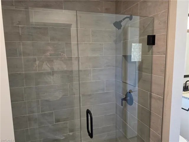 Glass-enclosed shower featuring large format tile surround, matte black shower fixtures, and a coordinating matte black handle