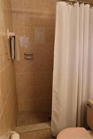 Enclosed shower with full-height beige tile surround, mosaic tile flooring, and integrated soap dish