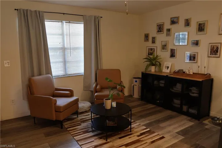 Living area featuring wood-finish flooring, a double window with blinds and drapes, and neutral wall tones