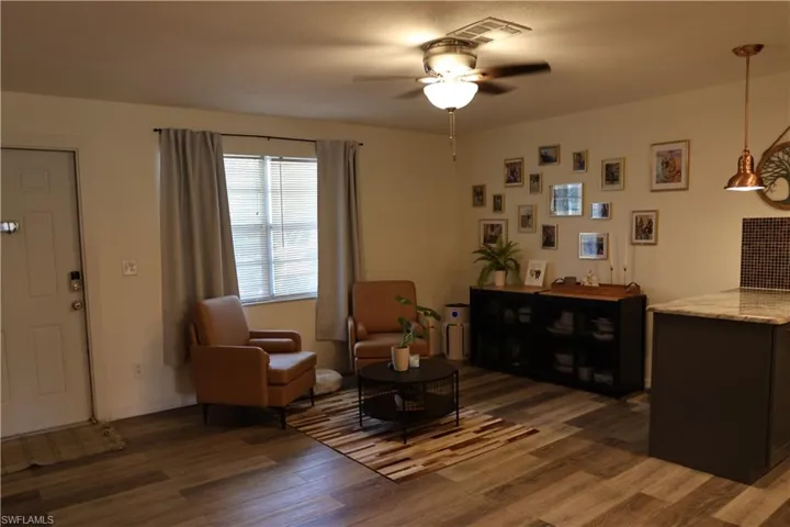 Open-concept living space featuring wood-finish flooring, a ceiling fan with integrated lighting, and a large window with blinds