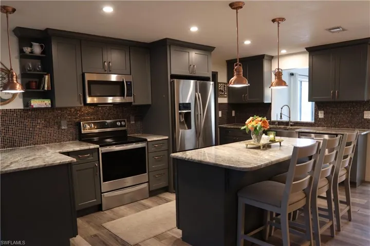 Kitchen featuring a central island with countertop seating, dark cabinetry, mosaic tile backsplash, and stainless steel appliances