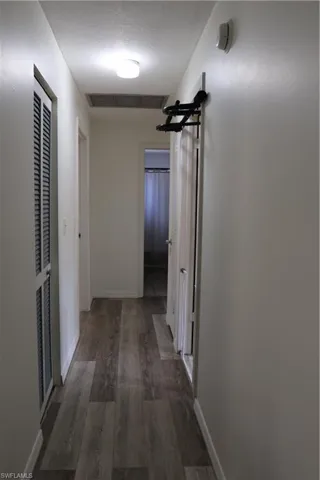 Hallway featuring wood-finish flooring, white painted walls, and ceiling-mounted lighting