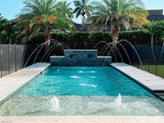 Rectangular swimming pool featuring a tiered stone-finish water feature, multiple water jets, and a baja shelf