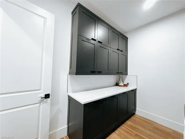 Laundry area featuring extensive dark cabinetry, light countertops, and wood-finish flooring