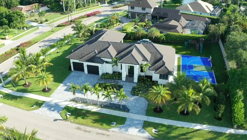 Modern single-story residence with a multi-car garage, extensive paver driveway, and a private sports court