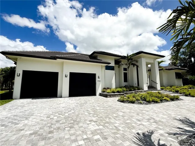 Contemporary residence featuring a paver driveway, two-car garage, and a covered entry with columns