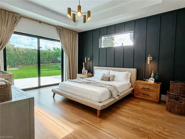 Spacious room featuring wood-finish flooring, a full-height sliding glass door leading to a green lawn, a dark accent wall with horizontal paneling, a horizontal window, and a modern chandelier