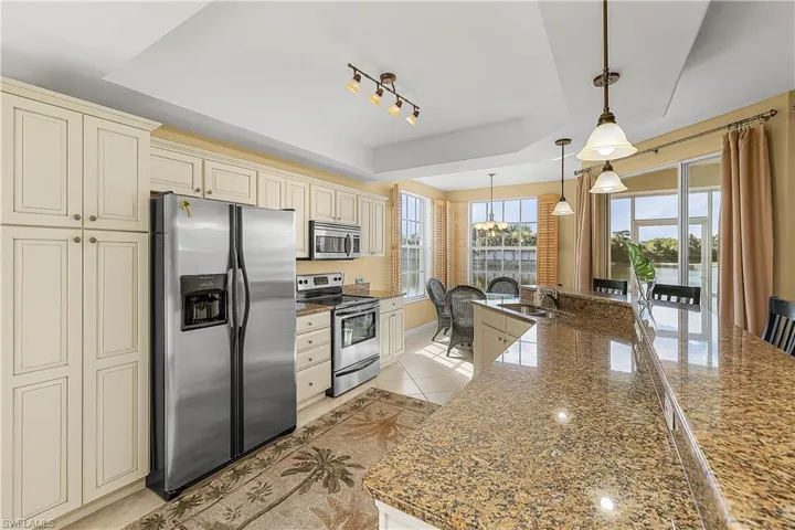 Kitchen featuring cream cabinets, appliances with stainless steel finishes, a tray ceiling, pendant lighting, and plenty of natural light