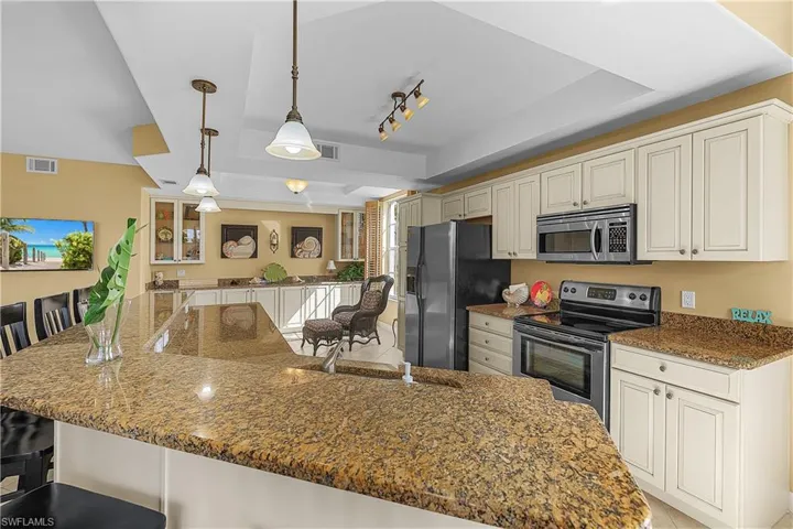 Kitchen featuring a breakfast bar, appliances with stainless steel finishes, a tray ceiling, and dark stone countertops