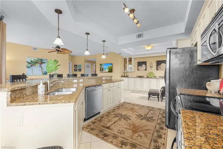 Kitchen with a tray ceiling, light stone counters, light tile patterned floors, stainless steel appliances, and decorative light fixtures