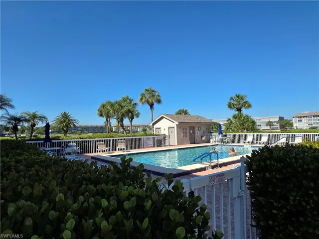 Outdoor swimming pool with a white perimeter fence, integrated pool steps, and a poolside utility building