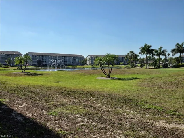Expansive green space featuring a fountain-adorned pond, mature palm trees, and multi-story residential buildings