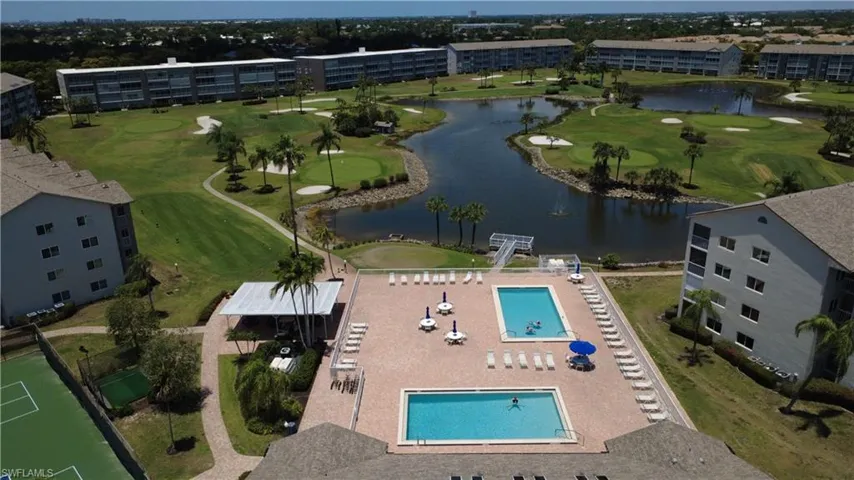 Expansive outdoor common area featuring two swimming pools, tennis courts, and a shaded pergola