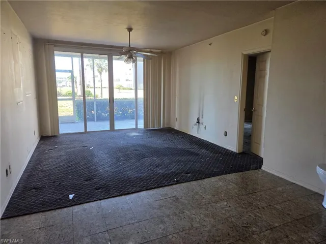Spacious interior featuring a ceiling fan, sliding glass doors, and a combination of patterned carpet and tiled flooring