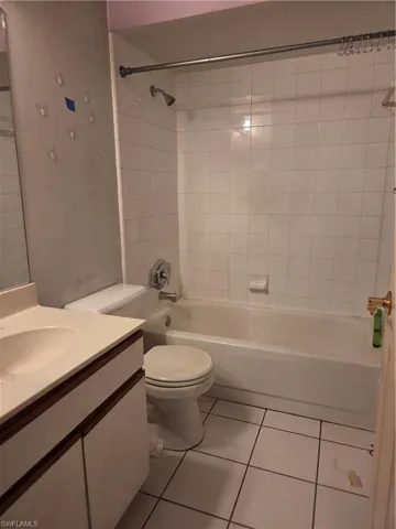 Bathroom featuring white square floor tiles, a white vanity with a single sink, a white toilet, and a white tub with white subway tile surround