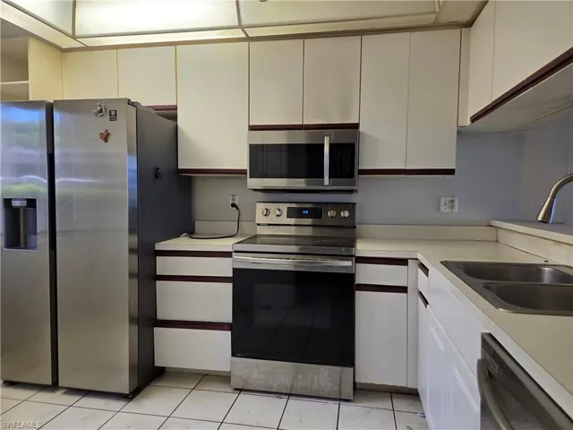 Kitchen featuring white cabinetry with dark trim, stainless steel appliances including a side-by-side refrigerator, over-the-range microwave, and electric range, and a double basin sink