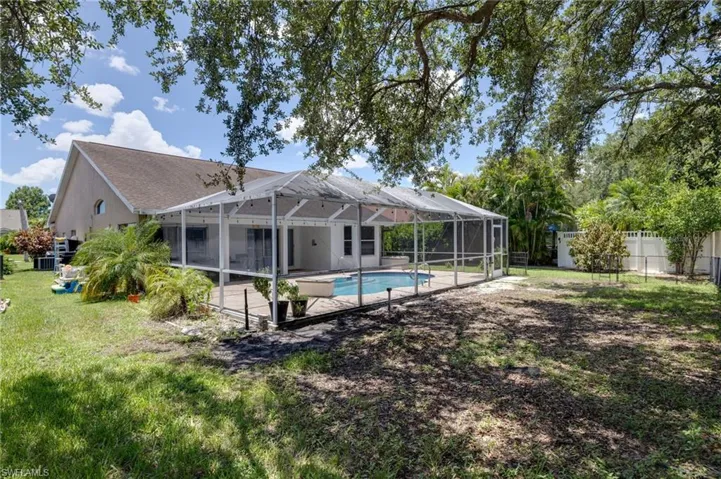 Expansive backyard featuring a screened-in pool enclosure, an in-ground swimming pool, and mature trees