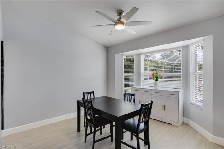 Bright interior space featuring a multi-paned bay window with white blinds, a contemporary ceiling fan with integrated lighting, light wood-finish flooring, and white baseboards