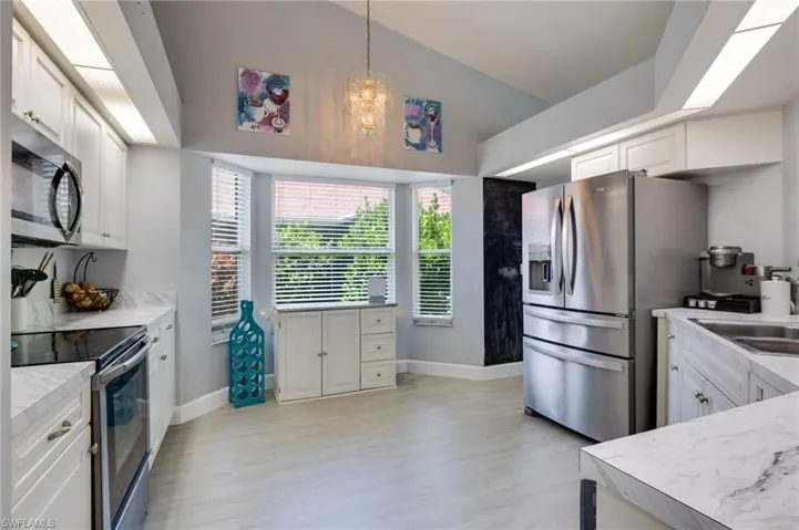 Kitchen featuring vaulted ceilings, bay window, wood-finish flooring, white cabinetry, and stainless steel appliances