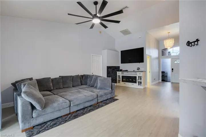 Spacious living area featuring light wood-finish flooring, vaulted ceilings, and a contemporary ceiling fan