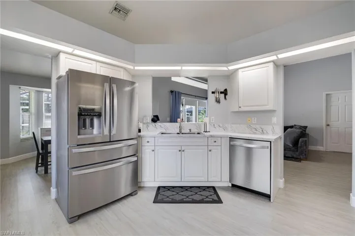 Modern kitchen featuring white cabinetry, stainless steel appliances, marble-look countertops, and wood-finish flooring