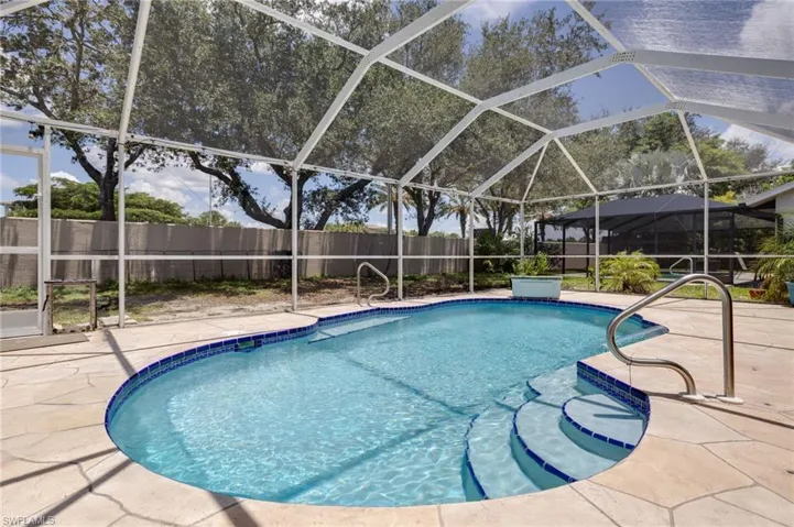 Screened-in outdoor living area featuring a freeform pool with integrated steps, blue tile accents, and stainless steel handrails