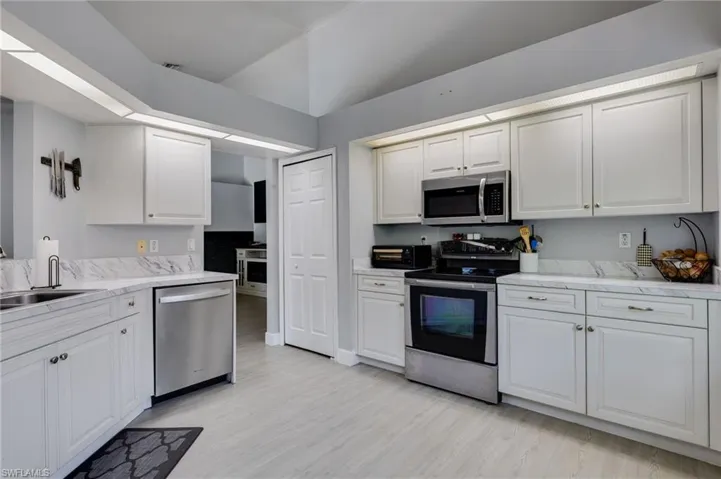 Kitchen featuring white cabinetry, light-toned wood-finish flooring, stainless steel appliances, marble-look countertops, and recessed lighting
