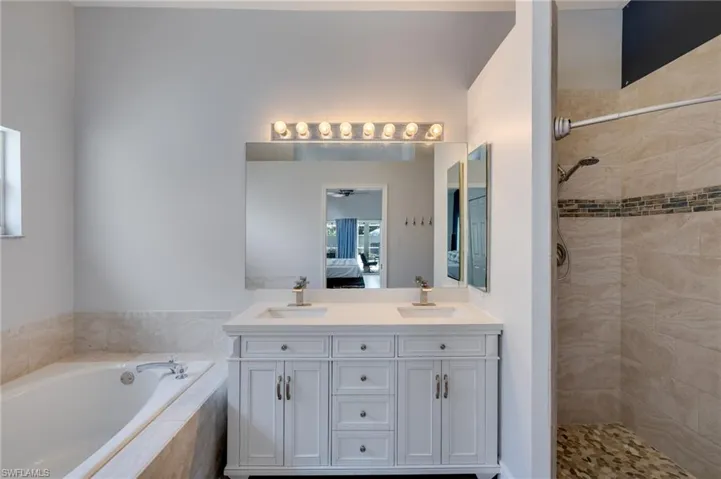Dual vanity with white cabinetry and integrated sinks, a large mirror, and overhead vanity lighting