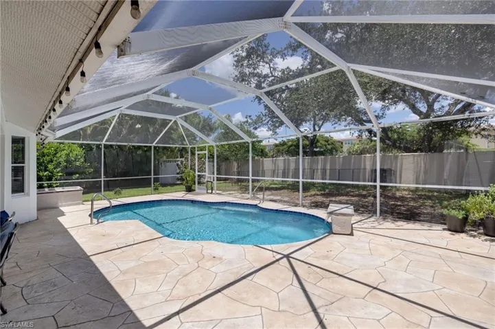 Screened-in pool area featuring a freeform swimming pool, extensive stone-look patio, and integrated lighting fixtures
