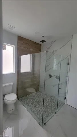 Bathroom with tiled shower, toilet, and tile patterned floors